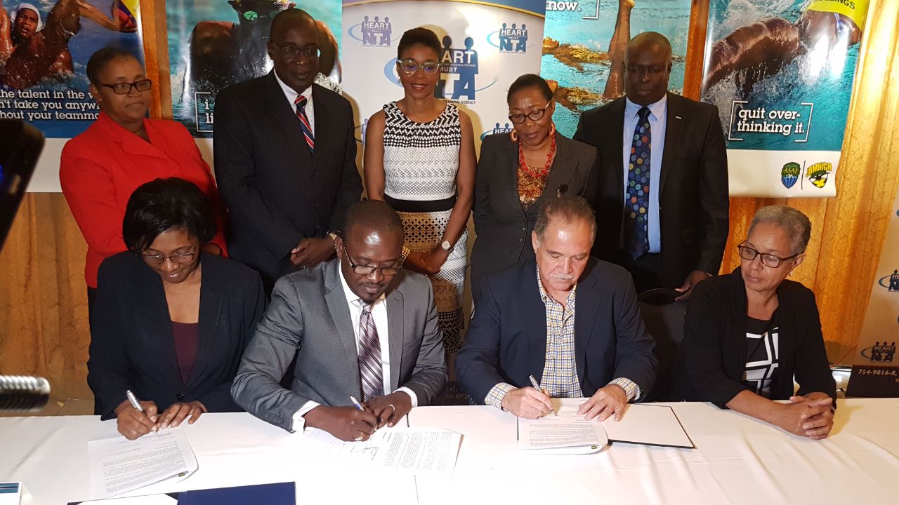 MOU being signed by (L – R): Dr. Janet Dyer Acting MD Heart Trust/NTA, Mr. Edward Gabbidon Chairman Heart Trust/NTA, Mr. Martin Lyn President ASAJ & Ms. Carol Thompson Honorary Secretary ASAJ. Looking on (L – R): Ms. Nicole Manning Senior Director Heart Trust/NTA, Minister Ruel Reid, Ms Tastey Blackman, Mrs. Florette Blackwood MCGES and Dr. Brian James Chairman CARIFTA 2018 Organising Committee